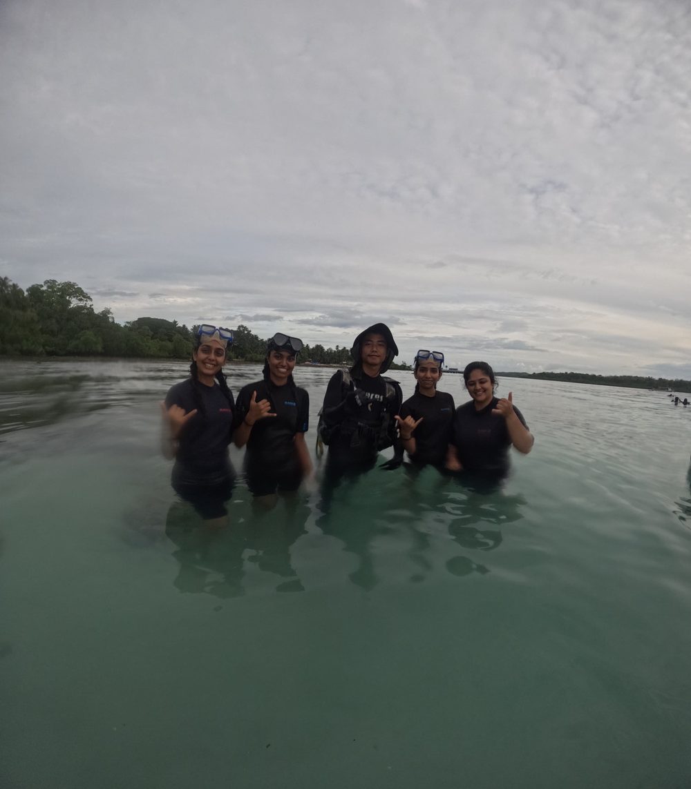 Five divers and their Scuba India guide smiling in the shallows at dusk, Havelock